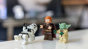 LEGO figures: a Stormtrooper does the Limbo, watched by Luke Skywalker and Yoda. They stand on a shiny surface, background is blurred.
