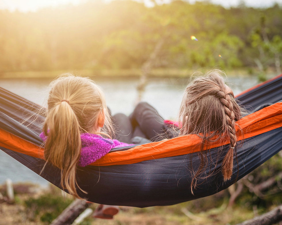 Two young women sitting in a hammock looking at a lake.