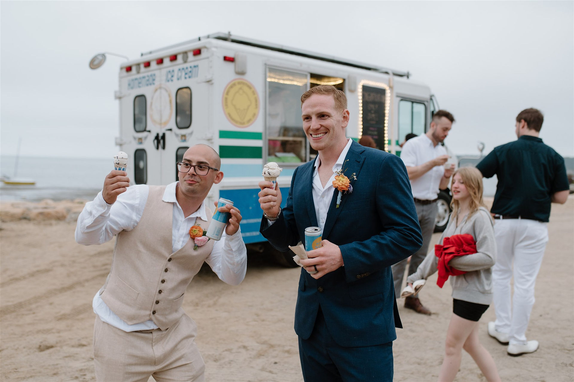 Two people holding ice cream cones in front of a food truck. They are dressed in formal wear, with other people in the background.