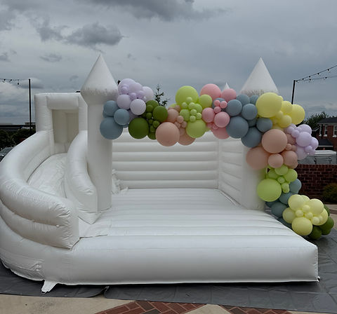 Premium white bounce house rental with pastel balloon garland for a birthday party in Dobson, NC by Halo Soft Play Co.