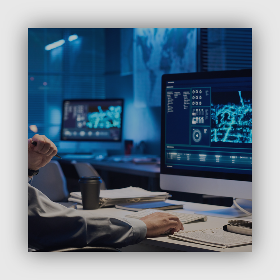 A person works at a desk with multiple monitors displaying data maps in a dimly lit office, creating a focused and tech-driven atmosphere.