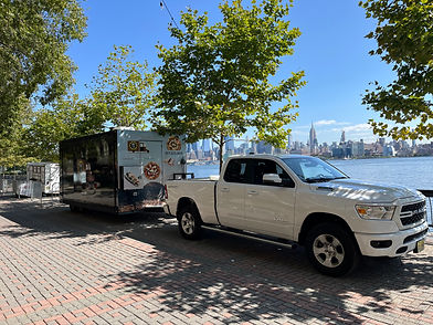 White pickup towing Culto Italiano catering trailer by river with city skyline for NJ wedding events
