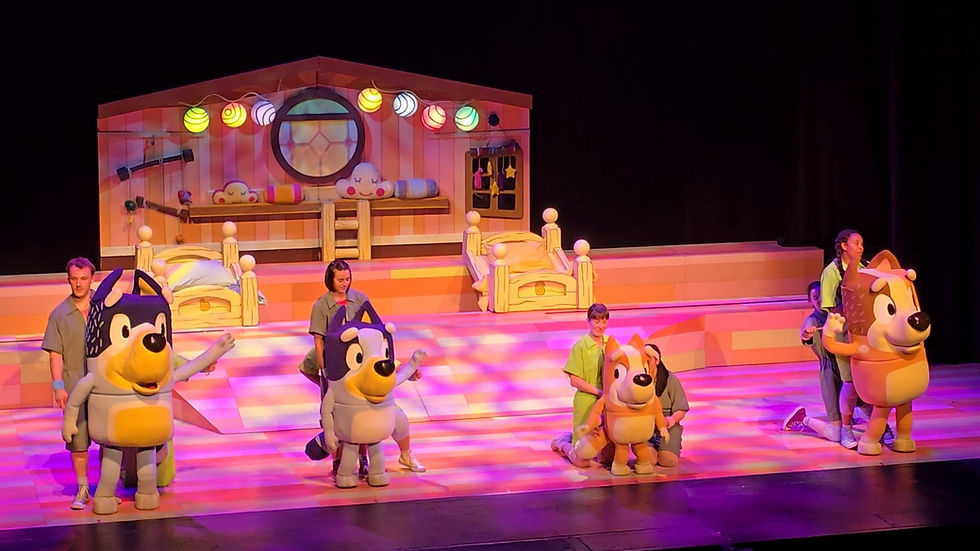 Bluey, Bingo and Bandit performing on stage during Bluey’s Big Play with puppeteers visible behind the characters and the Heeler family bedroom set in the background.
