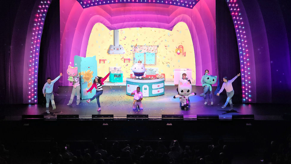 Performers on stage with colorful animal costumes, dancing under pink and purple lights. Confetti falls in a playful, whimsical setting.