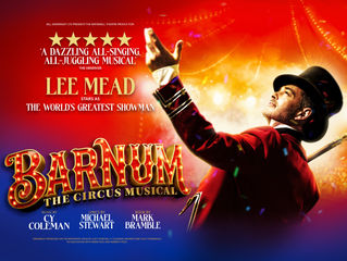 Man in red circus costume and top hat raises arm dramatically in spotlight. Text: Barnum: The Circus Musical. Vibrant red and gold colors.