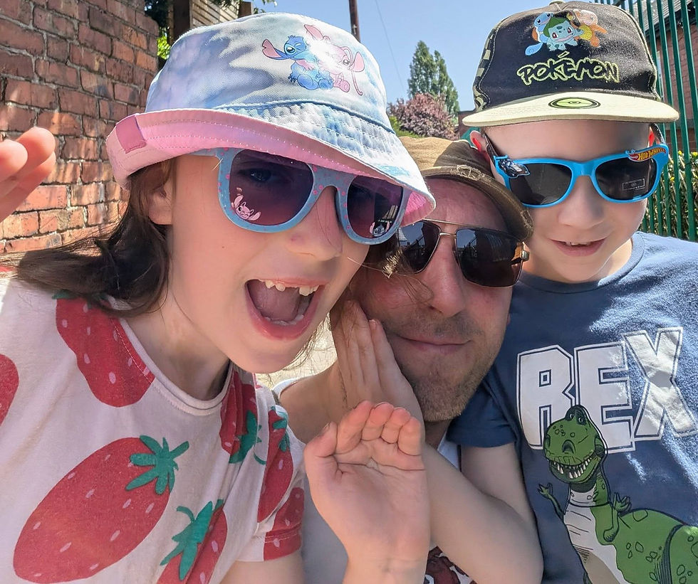 Two kids and a man smile in sunglasses and cartoon hats outdoors on a sunny day