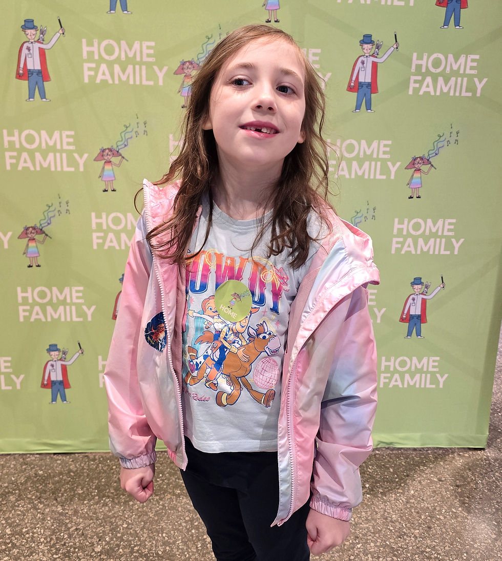 HOME Manchester - Smiling young girl in a pink jacket and Toy Story T-shirt stands before a green HOME FAMILY backdrop.