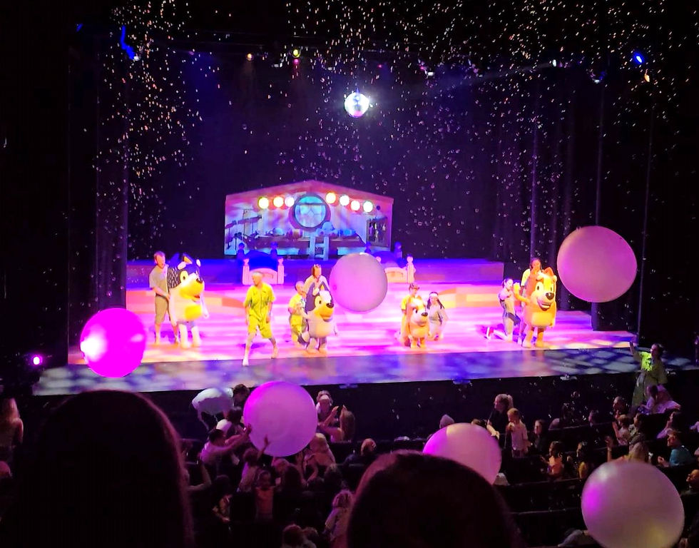 A stage performance of Bluey’s Big Play with colourful lighting, giant balloons, bubbles and audience members watching from the theatre seats.