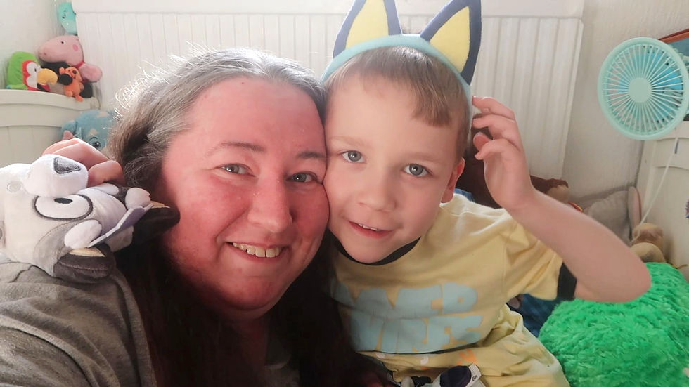 A smiling woman and young boy wearing Bluey-themed clothing and Bluey ears while posing together at home.