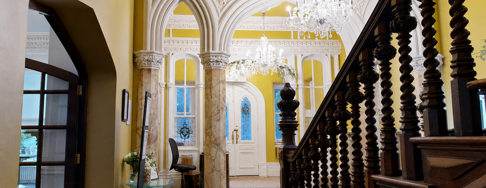 View through the entrance hall at Hollin House Hotel showing gothic arch detailing, carved wooden staircase, chandelier lighting and period architectural features.