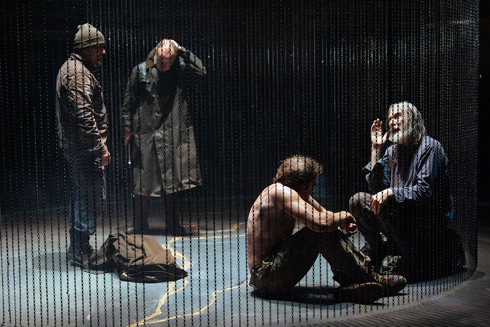 Performers in King Lear at the Royal Exchange Theatre surrounded by hanging metal chain curtains, with gold cracks visible across the stage floor.