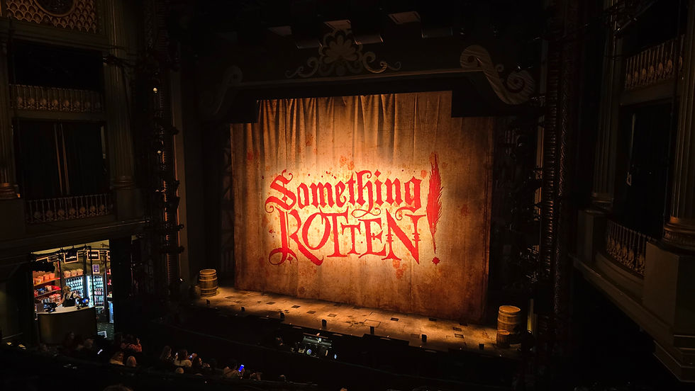 Something rotten Manchester - Theatre stage with a lit curtain reading Something Rotten!, viewed from audience seats in a dark ornate auditorium.