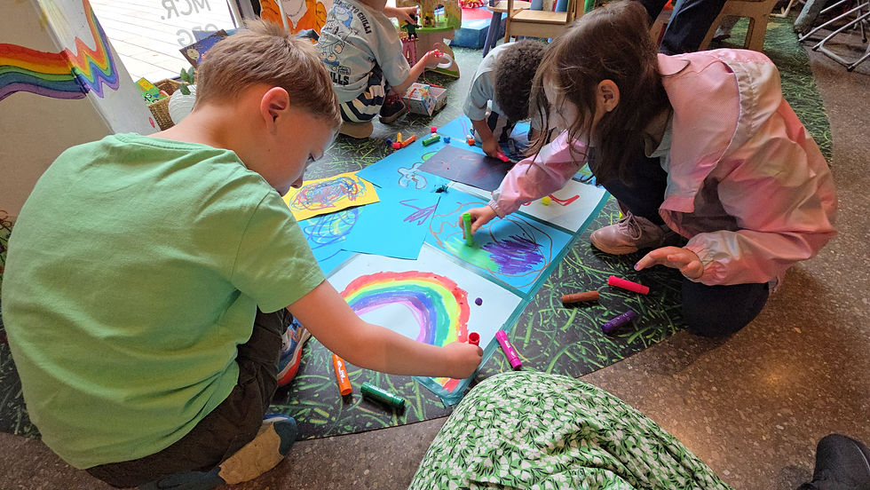 HOME Manchester - Children crouch on the floor drawing colorful rainbows and scribbles with crayons in a bright classroom, focused and creative