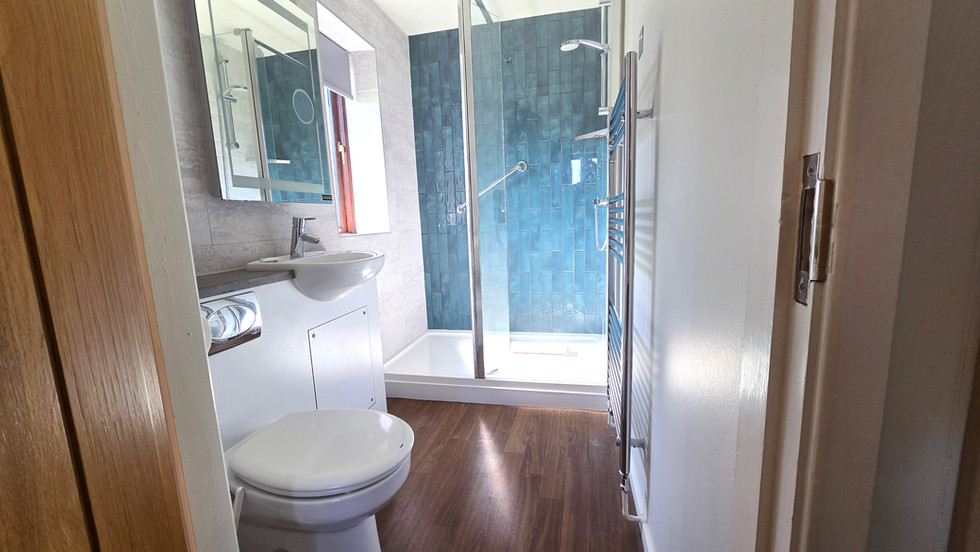 Modern shower room in the Sapphire Cottage at Ribby Hall Village featuring a walk-in shower, blue tiled wall, sink, toilet, and heated towel rail.