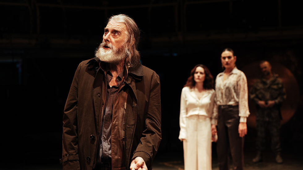 David Threlfall as King Lear wearing a dark coat, with three other cast members standing behind him during a dramatic scene at the Royal Exchange Theatre.