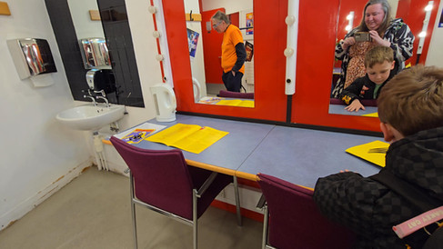 Lowry Backstage Tour - People in a red dressing room with mirrors and sink; a woman photographs a boy while others look at yellow pamphlets.