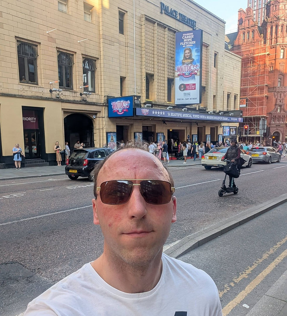 Man taking a selfie outside the Palace Theatre, with Waitress posters, traffic, and pedestrians on a busy city street.