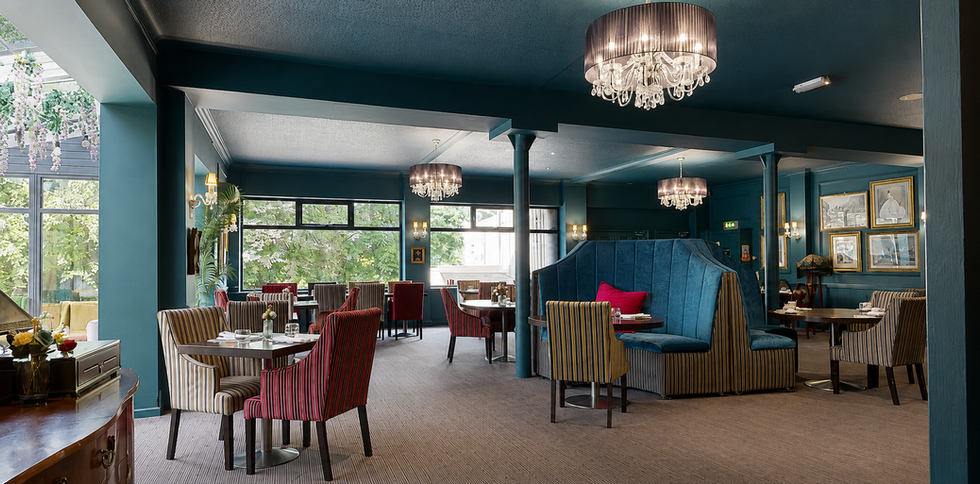 Elegant hotel restaurant dining area with teal walls, crystal chandeliers, striped chairs and cosy booth seating in a stylish lounge setting at Hollin House Hotel.