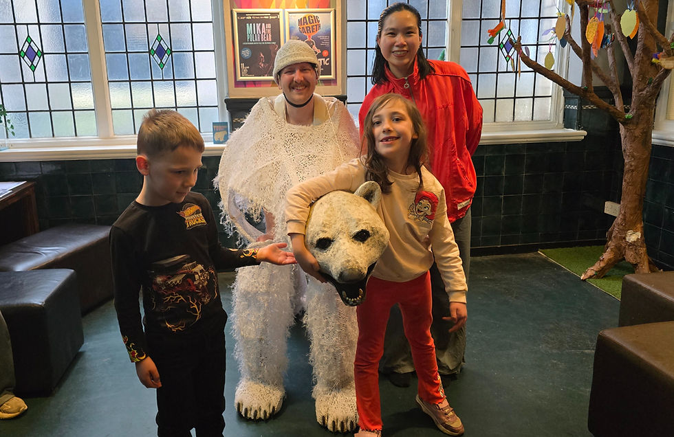 Group of people smiling indoors. A person in a polar bear costume, children nearby. Stained glass windows, posters in the background. Playful mood.