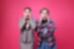 Freaky Friday The Musical -
Two surprised women hold their faces; one in a plaid suit, the other in a checkered shirt. Pink background enhances the shocked mood.