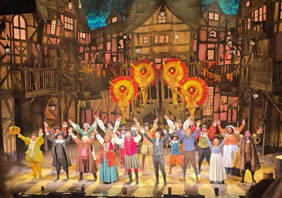 Something rotten Manchester -Cast bows on a Tudor-style stage, with dancers in yellow feather costumes on stairs and a cheering ensemble in front.
