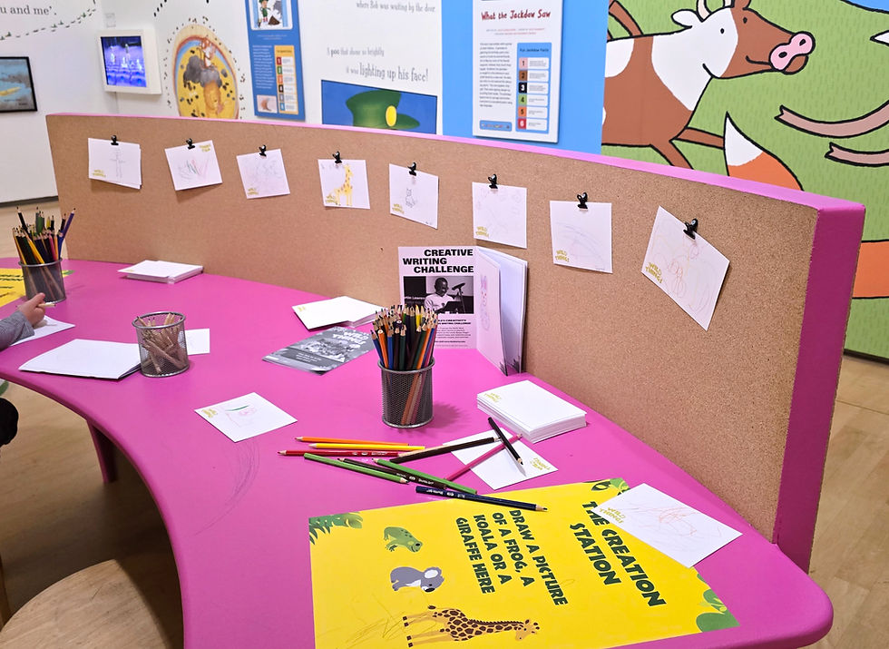 Wild Things Exhibition at the Lowry - Pink kids' art station with pencils, sketches, and signs reading Creative Writing Challenge and Draw a picture of a frog, koala or giraffe.