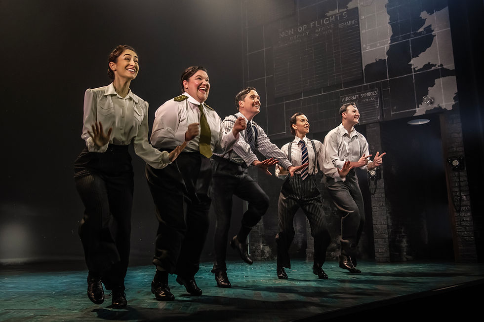 Operation Mincemeat UK Tour - Five people in vintage attire perform a lively dance on stage. A large map and flight board are in the background. Mood is joyful and vibrant.