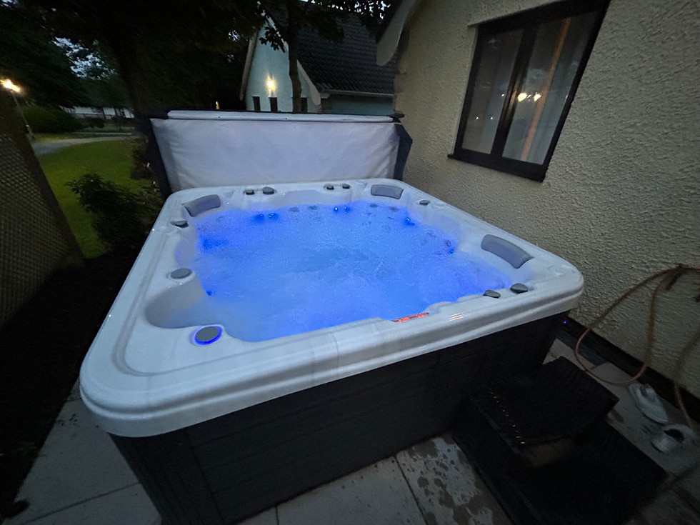 Evening view of the private hot tub at the Diamond Cottage glowing with blue lights during a relaxing family stay at Ribby Hall Village.