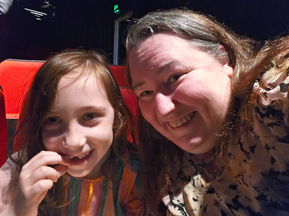 Smiling woman and young girl pose close together in red theater seats, with a dark background and warm, dim lighting.