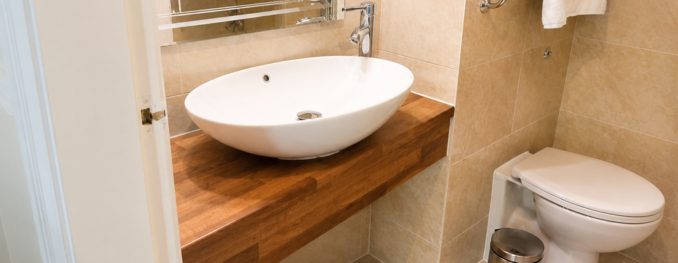 Modern family room bathroom at Hollin House Hotel with a large oval sink, wooden vanity unit, wall mirror, cream tiled walls and toilet with fresh white towels.