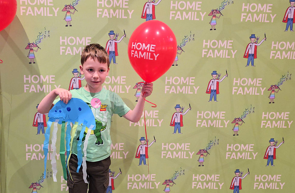 HOME Manchester - Boy holding a red balloon and blue jellyfish craft at Family Day Out, standing before a Home Family backdrop.