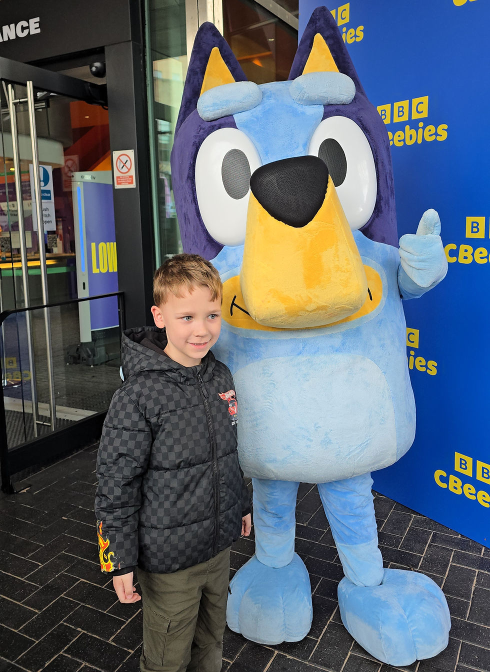 We Invented The Weekend Festival - Young boy poses beside a Bluey mascot outside a BBC CBeebies backdrop, smiling in a black jacket.