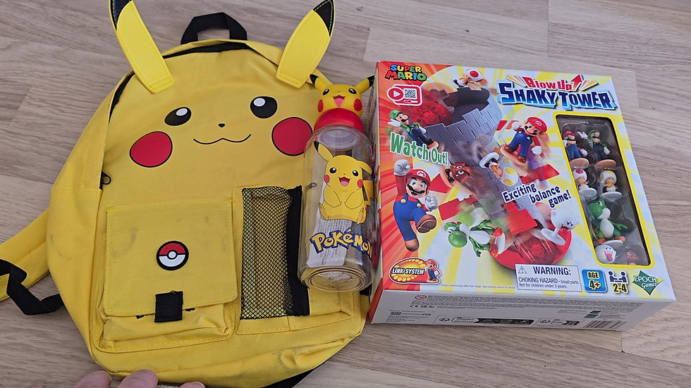 Yellow Pikachu backpack, Pokémon water bottle, and Super Mario Shaky Tower game box on wooden floor. Colorful, playful setting.