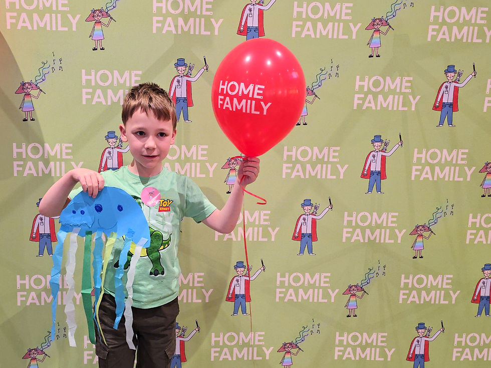 HOME Manchester - Boy holds a red HOME FAMILY balloon and blue jellyfish craft in front of a lime-green HOME FAMILY backdrop.