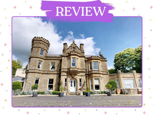 Grand stone mansion with turrets and bay windows under a blue sky, surrounded by trees and patio furniture.