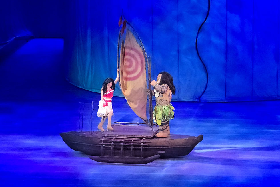 Disney On Ice Into The Magic - 
Two characters on a wooden raft stage under a blue spotlight, one in a red outfit with a brown sail, the other in a green leaf costume.
