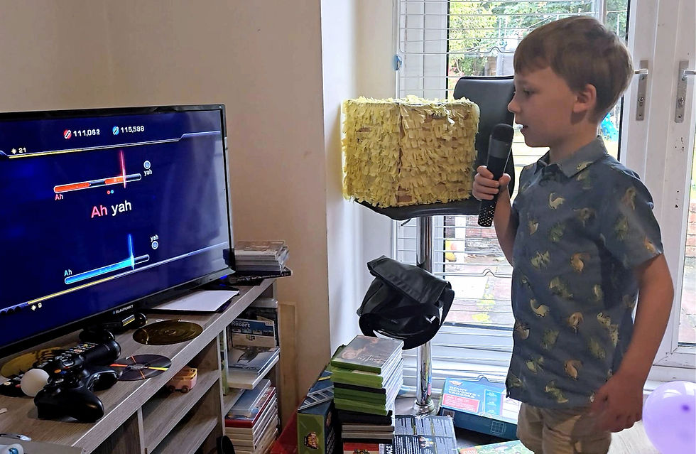 Boy sings into a microphone beside a TV karaoke game showing Ah yah in a bright living room.