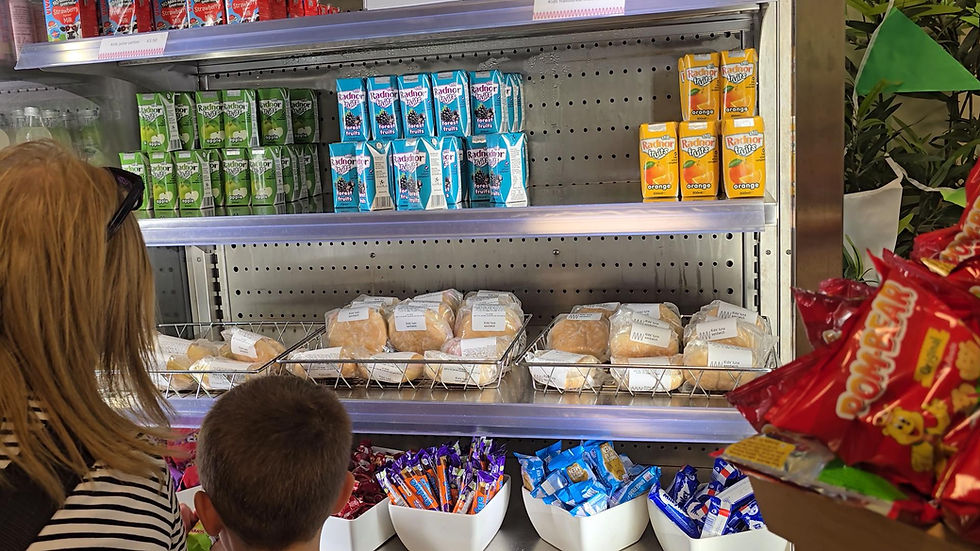 world museum cafe - People browsing a grocery display with juice cartons, sandwiches, and snacks. Bright packaging. Shelf labeled "Kids Juice."