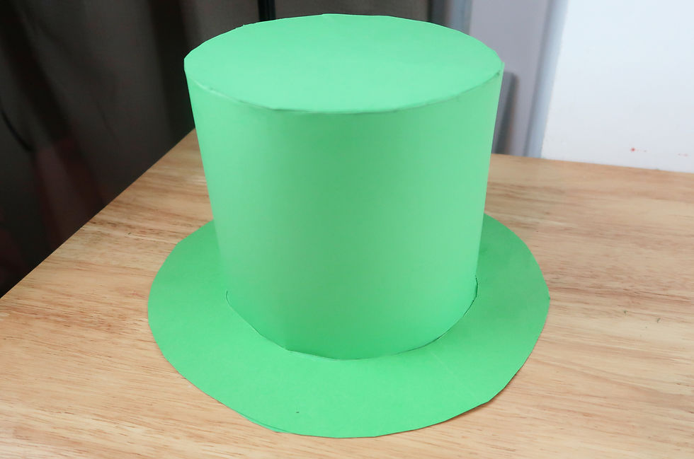 St Patrick’s Day DIY Leprechaun hat - A large, bright green top hat sits on a wooden table. The background is a brown curtain and a white wall corner.