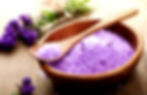 Purple bath salts in wooden bowl with spoon and flowers, relaxing spa.
