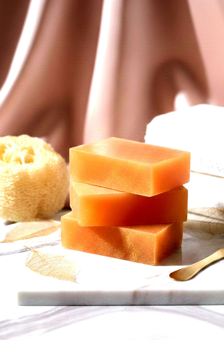 Three orange soaps stacked on a marble board, with a blurred background