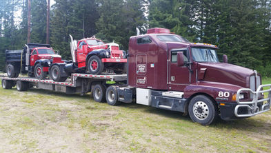 Maroon semi-truck hauls red vintage truck, "HAULING FREIGHT FORWARD" on door.