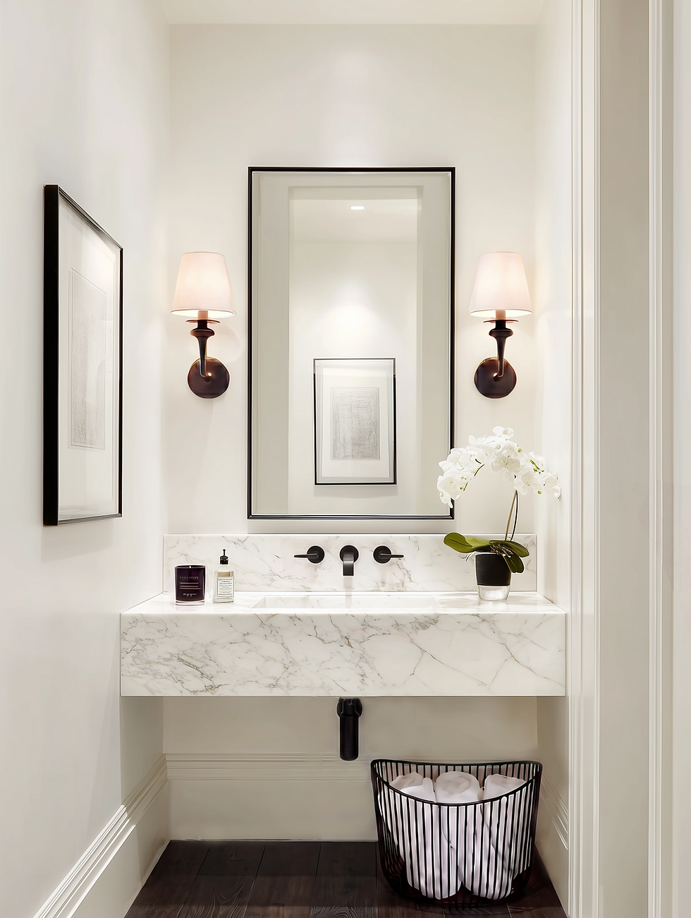 A classic elegant modern black and white powder room. Minimalist bathroom with marble sink, framed mirror, and wall sconces. Orchid and toiletries on counter. Basket with towels below. Elegant vibe.