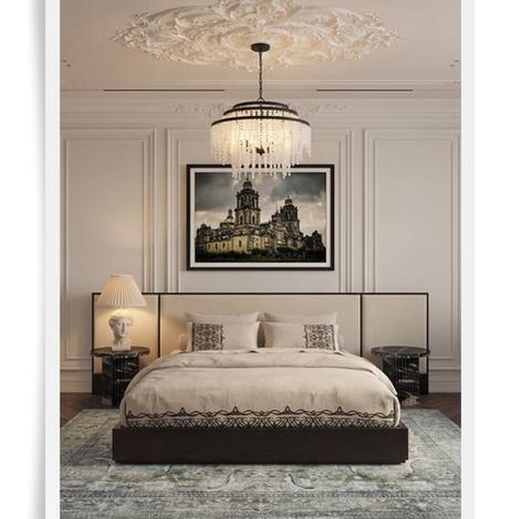 an elegant bedroom in a traditional space with high ceilings, white walls and ceiling with wall trim and moulding as well as a medallion on the ceiling with a large chandelier. the bedroom is white with black and white furnishings, a large oversized headboard bed with upholstered panels, black stone side tables, black and white embroidered bedding and photography of the mexico city opera house framed as art over the bed and a soft patterned rug on the floor over the wood flooring