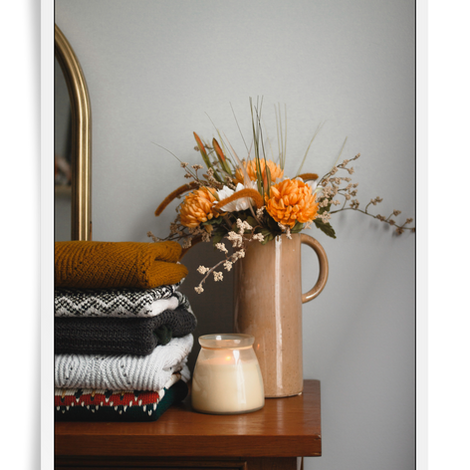 a console with cozy home decor including a stack of blankets and ceramic vase with dried flowers in autumn colors