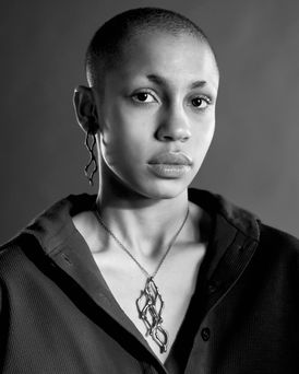 Black and white image of a young black woman with very short close cut hair, looking at the camera. She is wearing an open neck shirt and an organic dark oxidised silver necklace, She also modelled a pair of dark oxidised silver earrings.