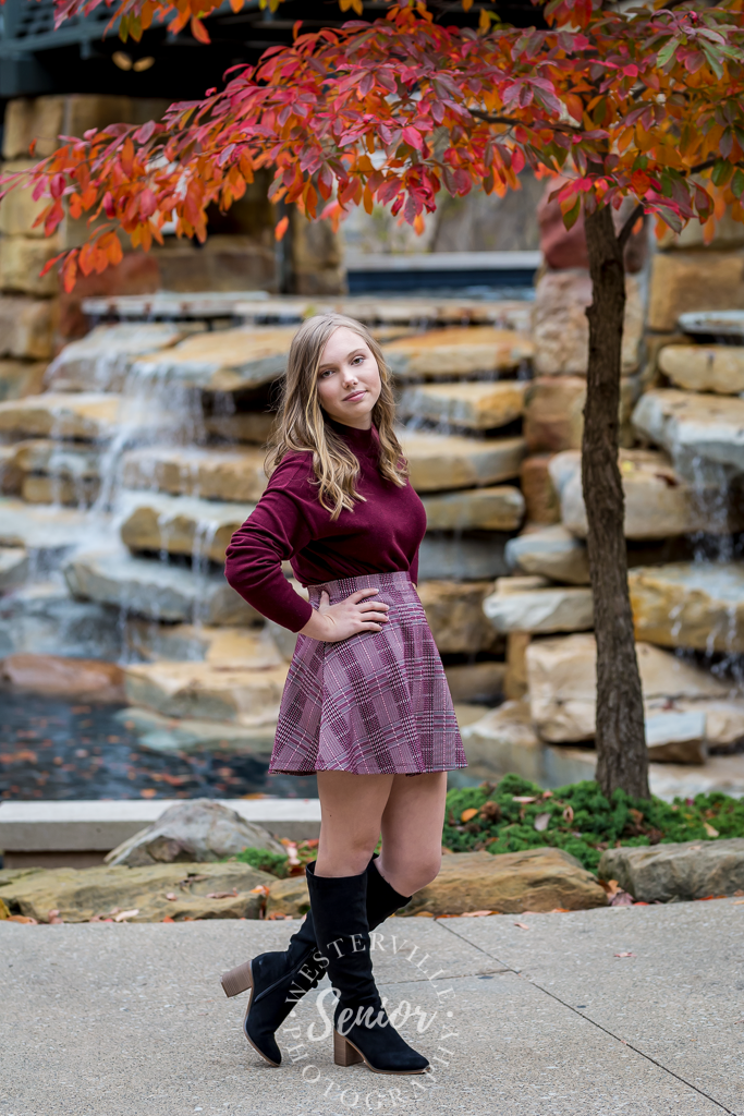 fall senior picture in Gahanna by waterfall and red tree and girl in skirt and boots