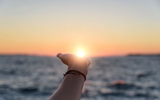 Female hand reaches for the sun at sunset against the background of the sea..jpg
