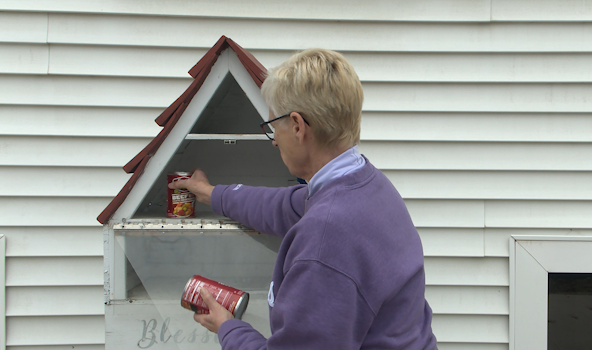 A person puts canned food into a blessing box.