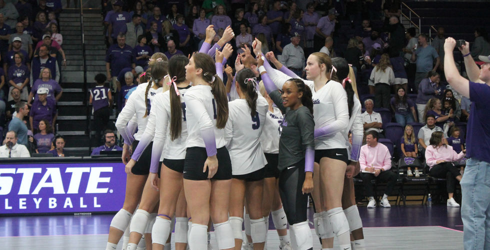 A K-State Volleyball player jumps in the air and prepares to spike a ball.